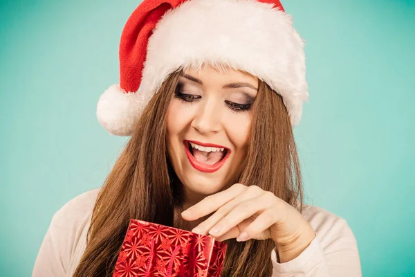 驚くべき女性を身に着けているサンタクラスの帽子彼女の手に置くクリスマス赤ギフトバッグ 上の青 — ストック写真