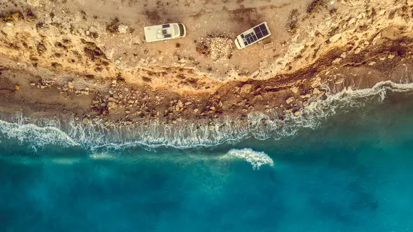 stock image Aerial view. Two camper vehicles with solar photovoltaic panels on roof camping on sea, coastal cliff in Spain. Caravan vacation.