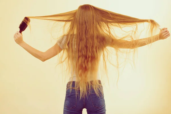 stock image Blonde woman with brush combing her very long hair. Teenage girl with bad hair care. Back view