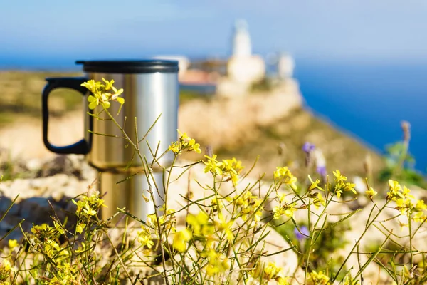 Thermal mug, thermos on nature. Travel destination, Mesa Roldan lighthouse in the background. Camping, vacation, lifestyle concept.