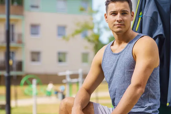 Handsome guy relaxing after outdoor workout. Fit man feeling healthy, enjoying sun. Exercising on public gym equipment in the open air.