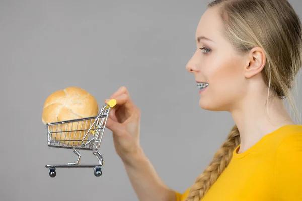 Buying gluten food products concept. Happy woman holding shopping cart trolley with bun breal roll