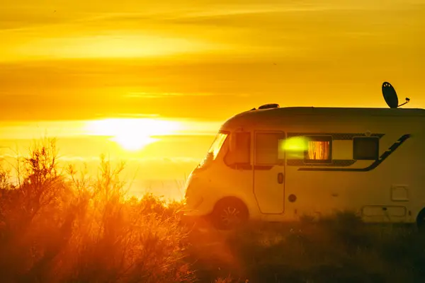 Sun rising over sea horizon and camper rv camping on beach seashore. Holidays in Spain, travel with motor home.
