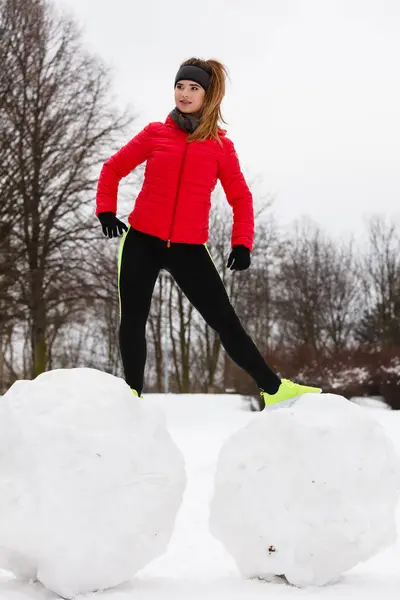 Outdoor sport exercises, sporty outfit ideas. Woman wearing warm sportswear training exercising outside during winter. Having fun while making snowman
