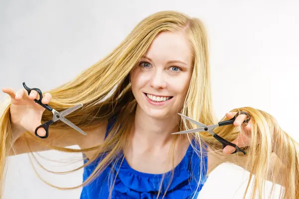 Girl with blowing long blonde hair holding scissors, showing work tools, normal and chunking shears. Making hairstyle, new hairdo. Haircare concept.