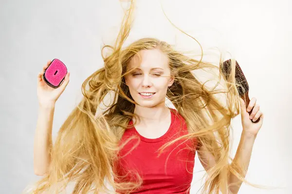 Blonde girl long blowing hair holds two brushes, one with natural bristles. Haircare, treatment concept.