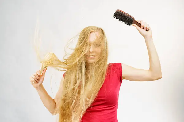 Blonde girl long blowing hair holds two brushes, one with natural bristles. Haircare, treatment concept.