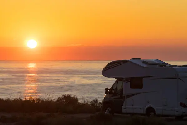 Sun rising over sea horizon, day break and caravan parking on beach sea shore. Travel with mobile home.