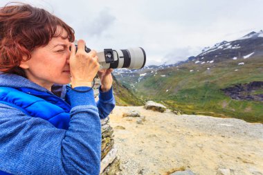Tourist woman enjoy mountains landscape, taking travel photo with camera. National tourist scenic route 55 Sognefjellet, Norway clipart