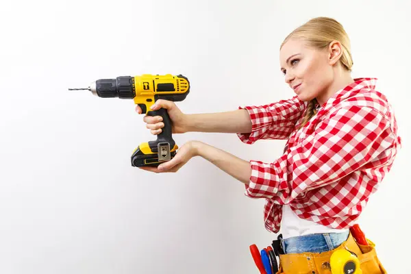ドリルを使用して若い決定女性が自宅の改装を行う 穴あけ工具の壁を持つ女性建設労働者 ロイヤリティフリーのストック写真