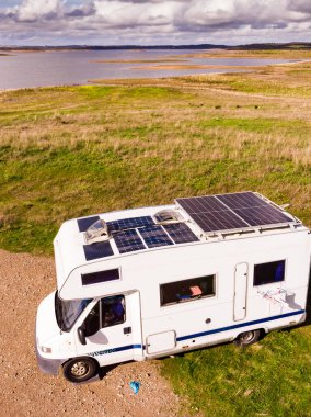 Aerial view of camper with many solar photovoltaic panels on roof camping on lake shore in Portugal. Renewable free energy. Caravan holidays. clipart