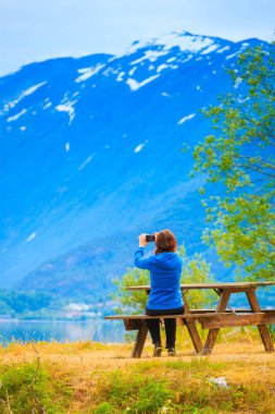 Tourism and travel. Woman tourist taking photo with camera, enjoying mountains lake Oppstrynsvatnet view in Jostedalsbreen National Park, Oppstryn (Stryn), Sogn og Fjordane county. Norway Scandinavia. clipart