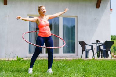 Woman using hoola hoop for slim waist, doing exercises gym outdoor in garden. Workout sport and training. clipart