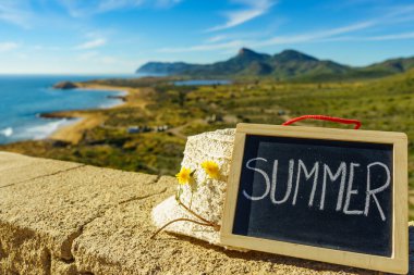 Black board with word summer against spanish sea coast. Landscape of Calblanque Park in Murcia Spain. Travel and holidays. clipart