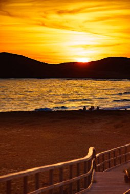 Sunset over beach seashore with wooden path to sea water. Cala Magre in Calblanque Regional Park, Murcia region Spain. clipart