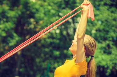 Young woman exercises outdoor in park, using gym accessory, resistance band, strap elastic. Staying fit and healthy. clipart