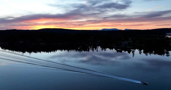 Recreational Fishing Boat Traverses Glassy Calm Sea Leaving a Wake in Front of Roche Harbor Washington USA Part of the San Juan Island Chain During a Vibrant Colorful Summer Sunset in September 2022