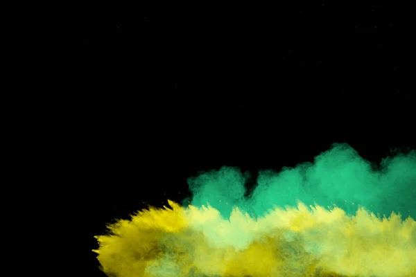 Yellow and green dust explosion on black background. Abstract yellow green powder splattered.