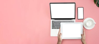 Çalışma alanı düz masa, pembe arka planda dizüstü bilgisayar, tablet, akıllı telefon kullanan kadın elleri. Boşluğu kopyala