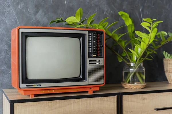Old orange TV on a wooden cabinet in the room of the house. Loft wall. Warm atmosphere. vintage set of tv equipments concept.