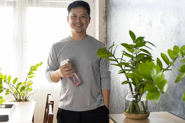 自宅でヘッドフォンの散水植物に満足している40歳のアジア人男性 家に植物を散水男 家事労働 — ストック写真