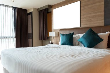 A large blank white framed poster in a black frame over the head of a bed in a luxury hotel bedroom. Stylish waiting area with wooden floors, 3D renderings simulated.