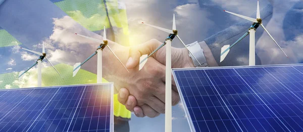 Solar energy panel photovoltaic cell and wind turbine farm power generator in nature landscape for production of renewable green energy is friendly industry. Business partners shaking hands.