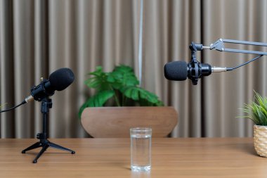 Sohbet etmek için iki mikrofon stüdyoda konuşmaya hazırlanıyor. Ev sahipleri için ahşap bir masanın üzerine bir bardak su. Katı renk perde arkaplanı.