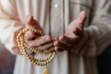 Müslüman bir adamın elleri dua ederken ve tespih tutarken yakın durun. Müslüman adam kutsal Kuran okuyor.