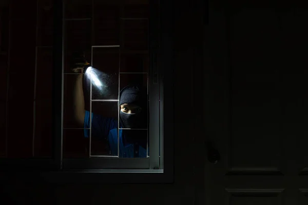 Burglar breaking in to home in night through window. Burglar at night with flashlight at window of the house. Thief Breaking House Window To Enter House