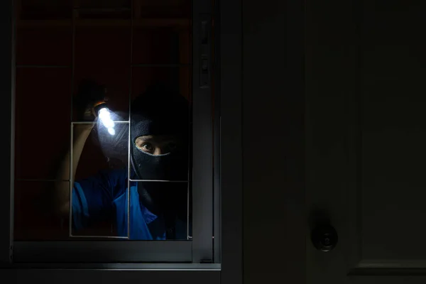 stock image Robbery Concept. Disguised burglar looking through glass in an apartment or office to steal something, using flashlight