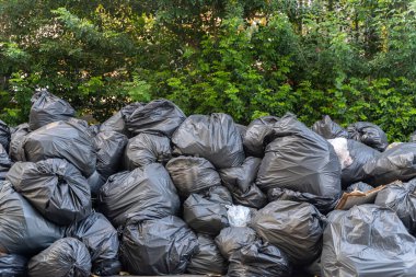 Siyah çöp torbası birikti. Kırışık plastik torbalar doku deseni. Yapraklardan oluşan bir duvara yığılmış bir sürü çözünebilir torba var..