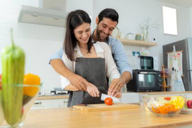 Young couple having fun while preparing breakfast together in a beautiful morning, cooking together, kitchen relationship, slicing tomatoes together.Love of a couple. clipart