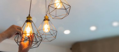 Bir elektrikçi tavana spot ışıkları yerleştiriyor. Apartmanın ışığını değiştirirken enerji tasarrufu ve ucuz akkor lamba arasında seçim yapan tamirci.