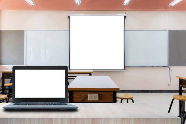 Dizüstü bilgisayar ön planda. Modern konferans odasında büyük pencereli projektör ekran tuval. Yan görüş. Boş sınıf veya sunum odası içi masalar, sandalyeler ve beyaz tahtayla dolu.