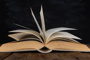 Karanlık masanın üzerinde açık İncil kitabı. Karanlık ve gölgelerin arasındaki parlak ışıktaki Yeni Ahit 'in sade görüntüsü ahşap masadaki açık antik kitap görüntüsü.. 