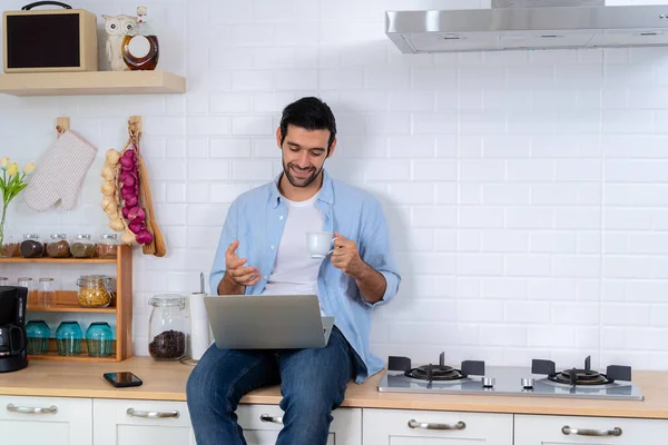 Gain new knowledge via video conferencing. Self-education, e-learning concept. Handsome man using a laptop pc in the kitchen, calling online indoor, business webinar training, studying online.