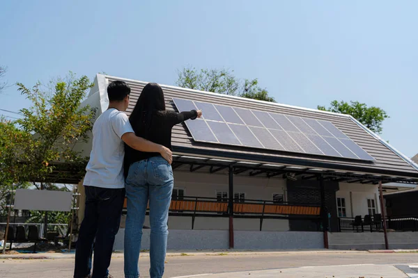 stock image Family uses renewable energy system with solar panel. Rear View Of A Young Couple Standing In Front Of Their New House, a solar module on a sunny day, copy space, side view
