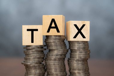 Yığınla bozuk para üzerinde tahta bloklar olan vergi konsepti. Kelime vergisi, tahtadan küplere, birikmiş paralara ve karanlık arka plana yazıldı. Ödeme vergisi kavramı - madeni para yığınlarındaki tahta bloklar