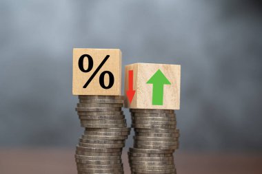 The concept of increasing or decreasing interest rates. Wooden cube with percentage icon Up and down symbols are placed on piles of coins on a dark background. clipart