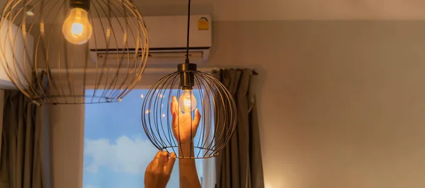 Woman's hands changing light bulb. Close-up. A hand changes a light bulb in a stylish loft lamp. Spiral filament lamp. Modern interior decor. Panoramas have empty spaces that can contain image text.