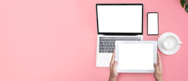 Pastel pembe ofis masası üst kahve fincanı, dizüstü bilgisayar kullanan kadın elleri, akıllı telefon ve tablet ekranı tutan, reklam için boş alan, panoramik resim tarzı.