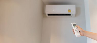 Beyaz klima kumandası bir insan eli tarafından bir odadaki klimayı açmak ve ayarlamak için kullanılıyor. Klimanın sıcaklığını uzaktan ayarlıyorum. Klima sistemi