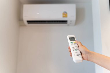 Beyaz klima kumandası bir insan eli tarafından bir odadaki klimayı açmak ve ayarlamak için kullanılıyor. Klimayı uzaktan kumandayla kontrol et..