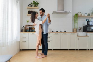 Evdeki mutfakta dans eden güzel genç bir çift. Modern mutfakta dans eden mutlu, genç çift gülümseyen karı koca, yıldönümünü kutluyor ve eğleniyor..