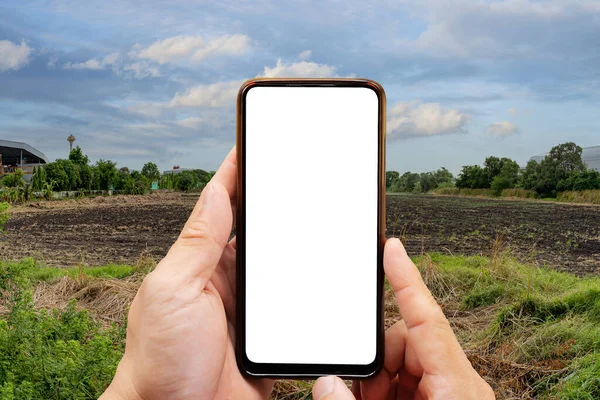 Cropped image of businessman using smartphone. Empty dry cracked swamp reclamation soil, land plot for housing construction project and beautiful blue sky. Land for sales landscape concept.