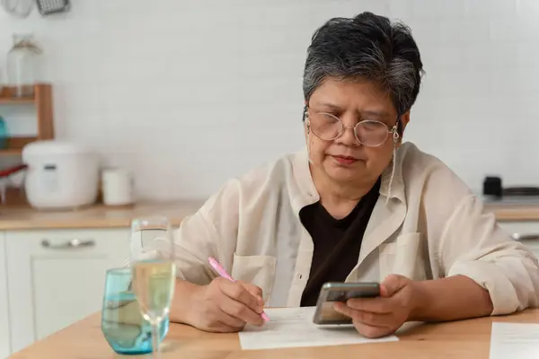 Senior old woman writing down letters on a piece of paper, record. Cheerful old woman writing on paper, calculating bill payment. Close-up of an older woman\'s hand signing a paper