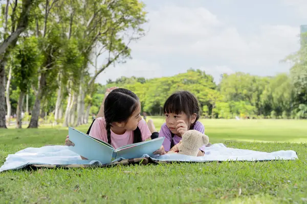 Two children lie down and read a book in the garden of young sibling girls lying in the park and reading a book on a warm summer day. Beautiful Asian woman lying down and reading a book in the park.