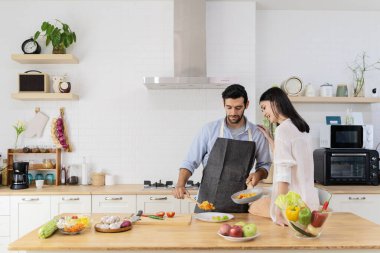 Mutfakta genç ve güzel bir çift, iki kişilik bir aile, mutfak masasında oturan bir kadın ve erkeğin lezzetli makarna yapmasına yardım ediyor..
