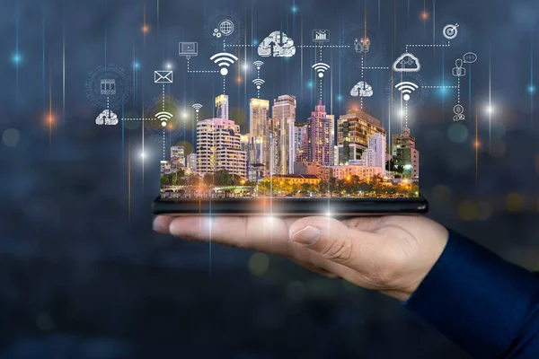 Smart city technologies concept with digital tablet and night megapolis city skyscrapers with digital cloud icons on human hand at blurry skyline background.